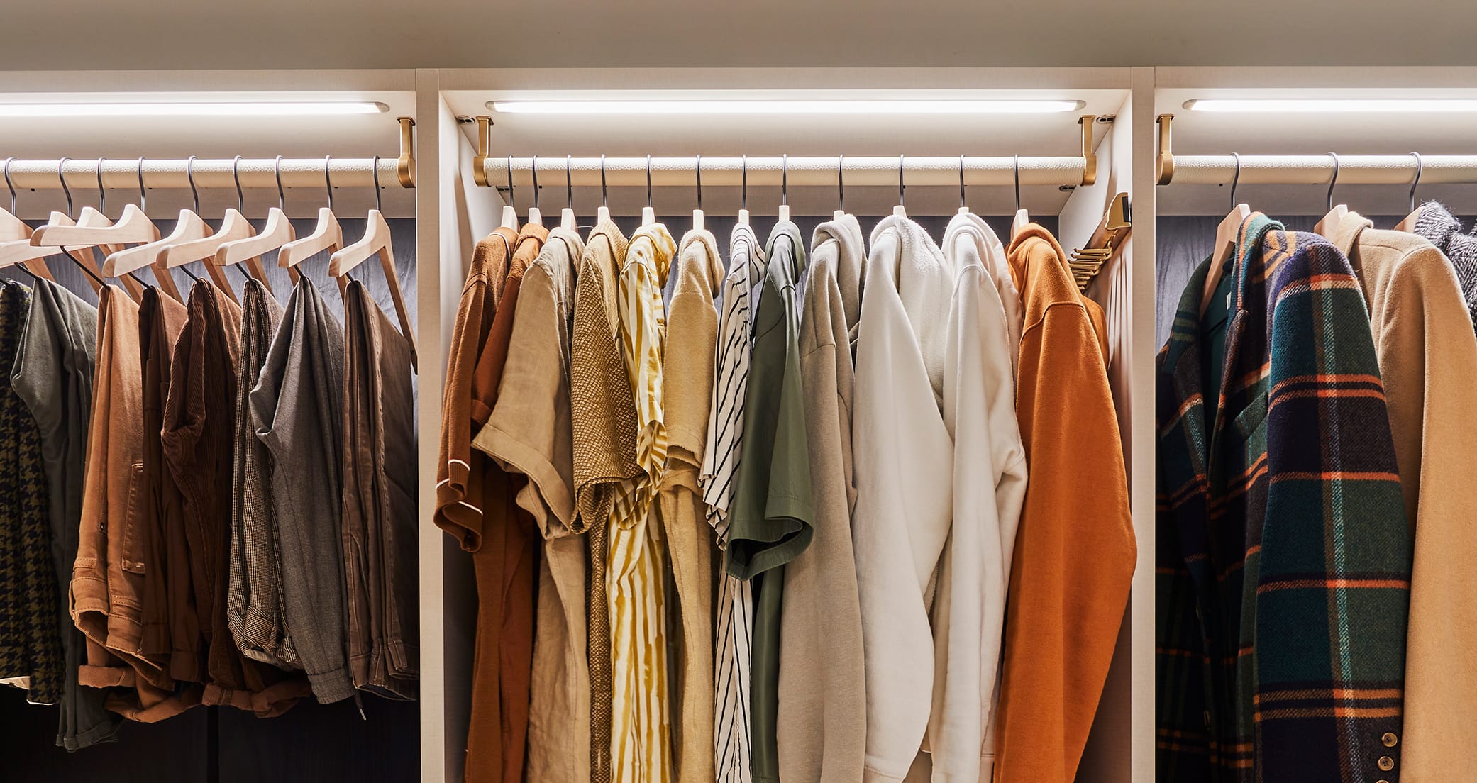 Custom reach in closet showing clothes ordered by color and category with LED lighting feature created by California Closets