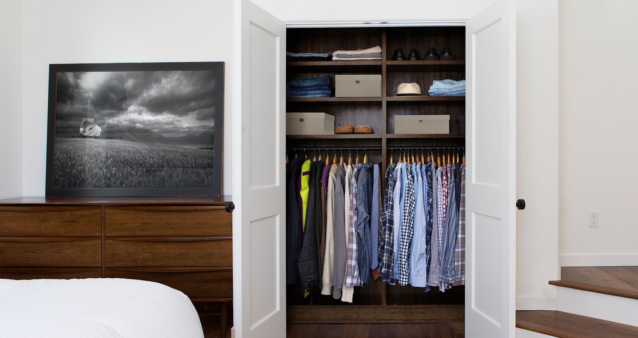 Small reach in closet for a bedroom with extra open shelving for storage in dark wood finish by California Closets