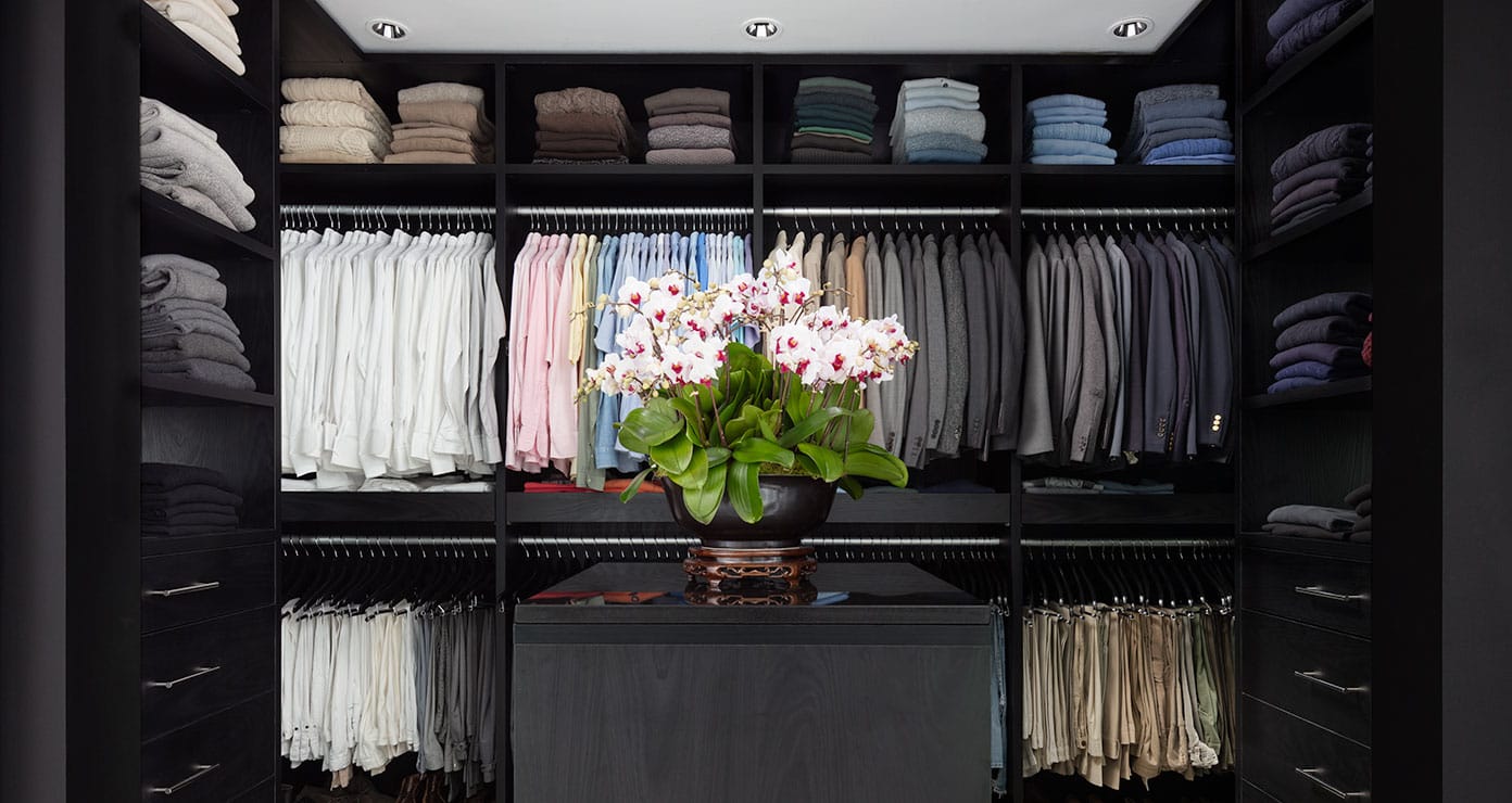 Dark wood finish walk in layout with custom shelving and wardrobe hanging space by California Closets
